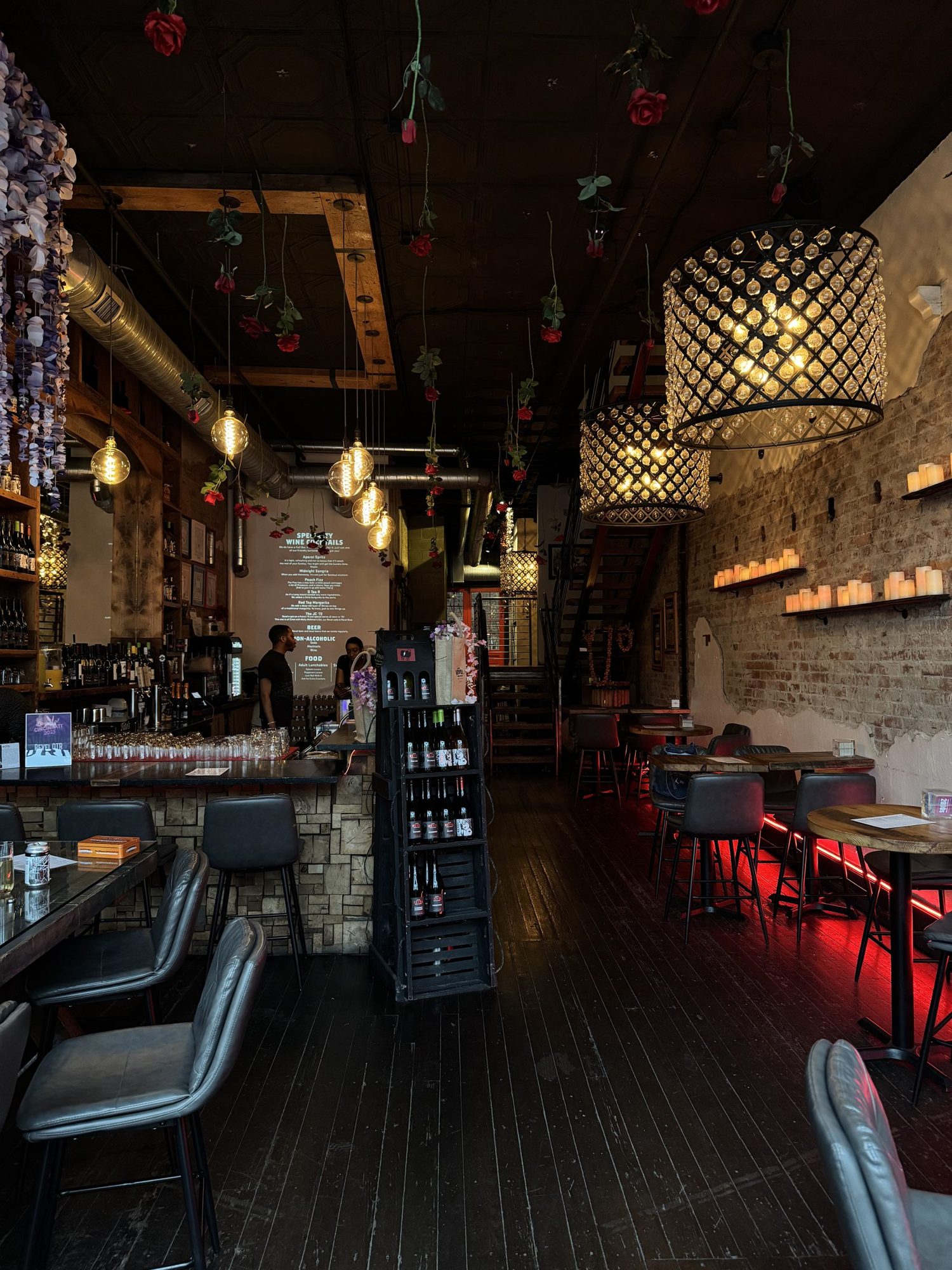 Revel OTR interior at night — hanging roses, crystal chandeliers, candlelit brick wall and red neon along the seating