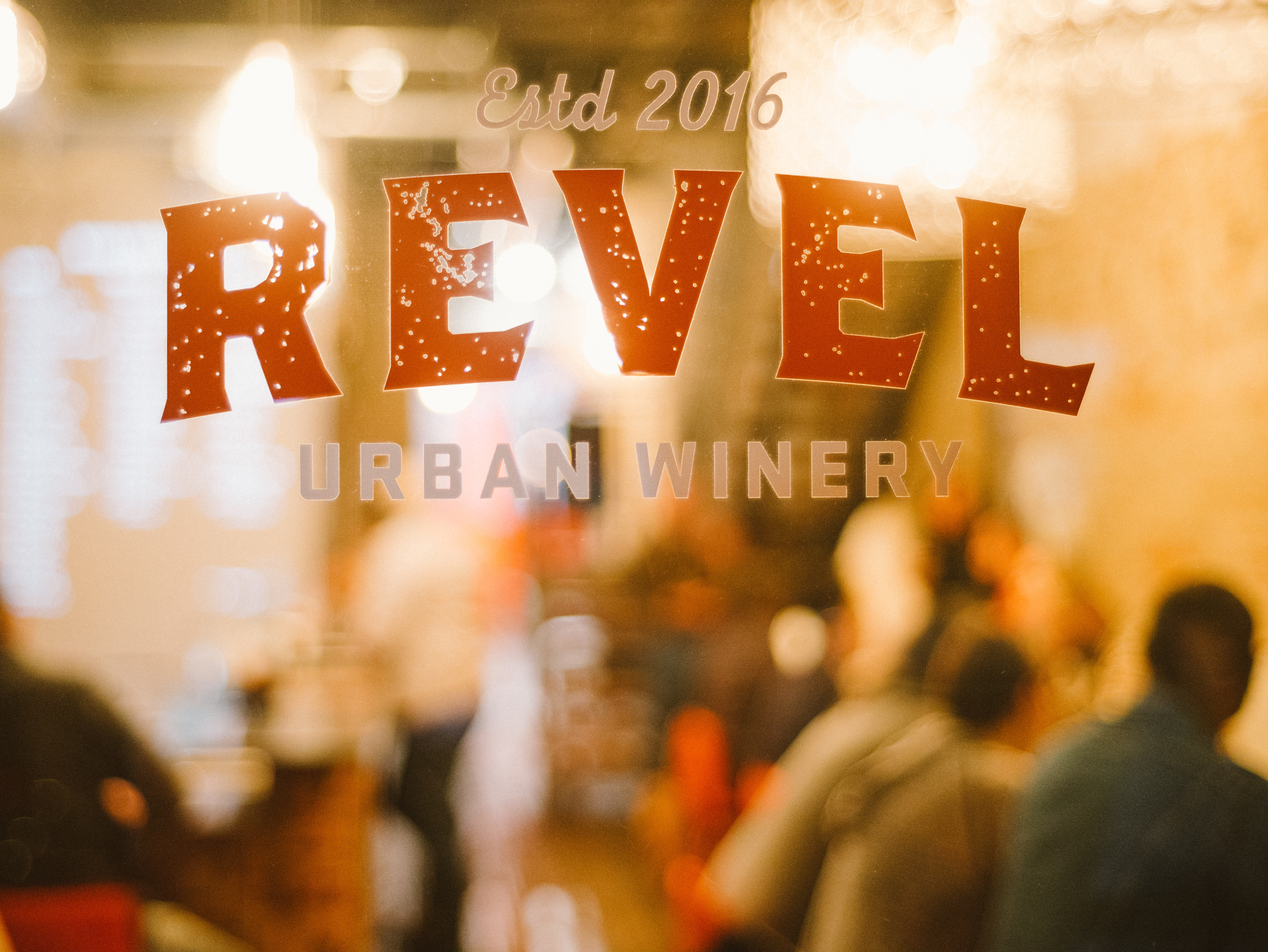 Estd 2016 Revel Urban Winery logo etched on the front glass, taproom visible behind
