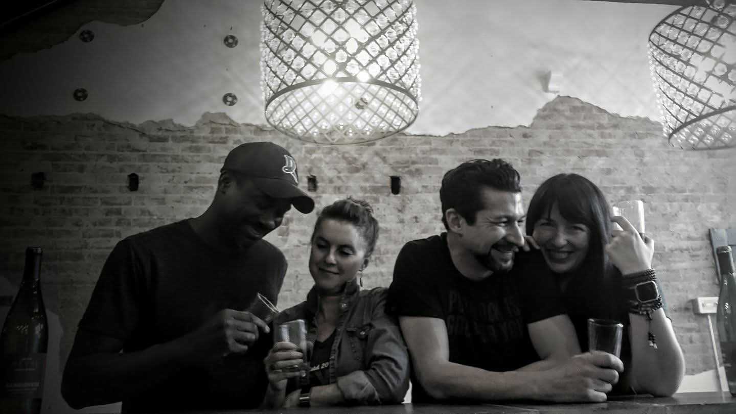 Black and white photo of four friends laughing over drinks at the Revel bar counter